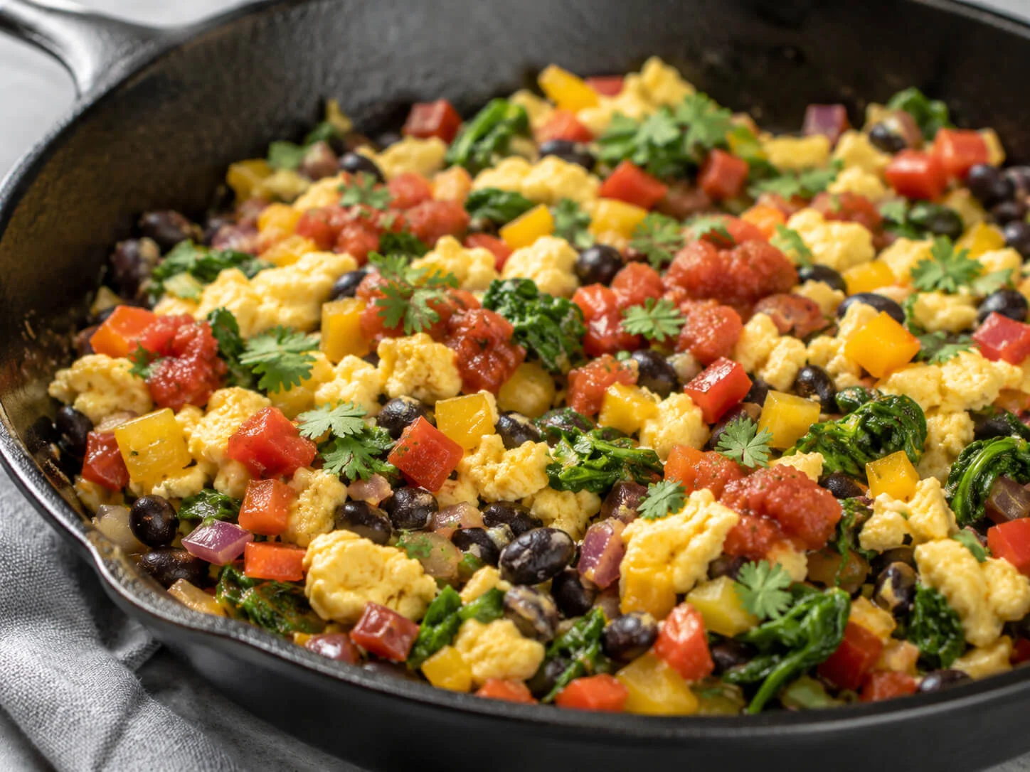 Breakfast taco egg filling with scrambled eggs, black beans, spinach, peppers, onion, cilantro, and salsa in a skillet