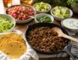 Healthy beef taco night spread with lean ground beef, tortillas, lettuce, salsa, avocado, cilantro, lime, and yogurt sauce