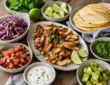 Healthy chicken taco night spread with grilled chicken, tortillas, cabbage, salsa, avocado, lime, and yogurt sauce