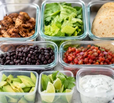 Healthy taco meal prep containers with chicken, tortillas, lettuce, beans, avocado, salsa, cilantro, lime, and yogurt sauce