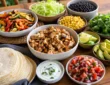 Healthy taco night spread with tortillas, chicken filling, fresh toppings, avocado, salsa, beans, and vegetables