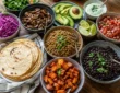 Vegetarian taco night spread with black beans, sweet potatoes, mushrooms, lentils, tortillas, avocado, salsa, cabbage, cilantro, and lime